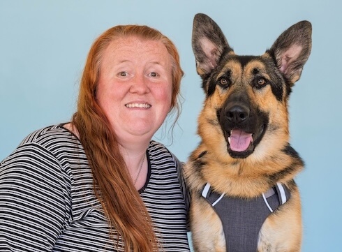 Christina and black & tan German Shepherd guide dog Zeppelin pose against a light blue background for their team portrait