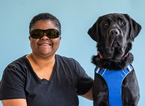 Elnora and black lab guide dog Poncho pose against a light blue background for their team portrait