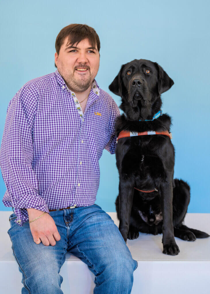 Noble and black Lab guide dog Sparky pose against a light blue background for their team portrait