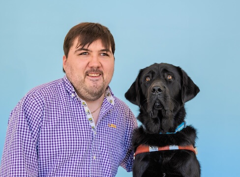 Noble and black Lab guide dog Sparky pose against a light blue background for their team portrait
