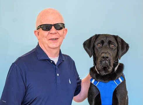 Willie Lab and black Lab guide dog Bono sit side by side for their team portrait against a blue background