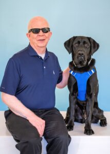 Willie Lab and black Lab guide dog Bono sit side by side for their team portrait against a blue background