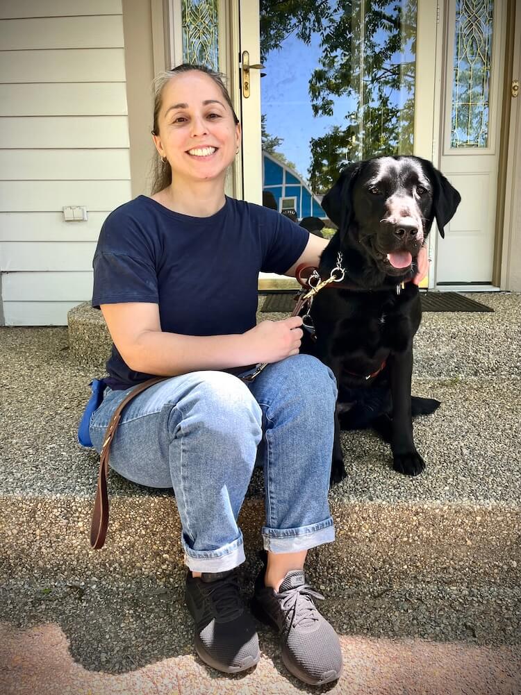 Chelsea and black Lab guide dog Steffie sit together on the step of a home's entrance