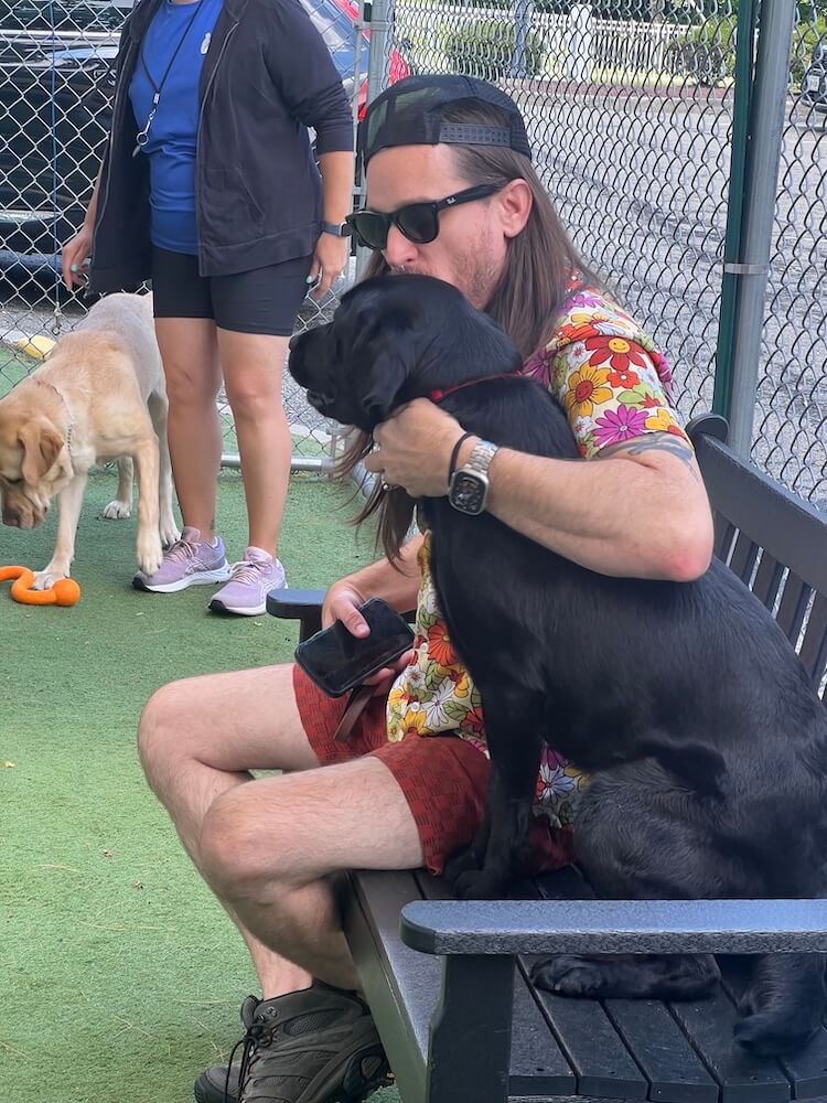 Kevin and guide dog Yahtzee share a sweet moment sitting together on a bench in the campus grounds.