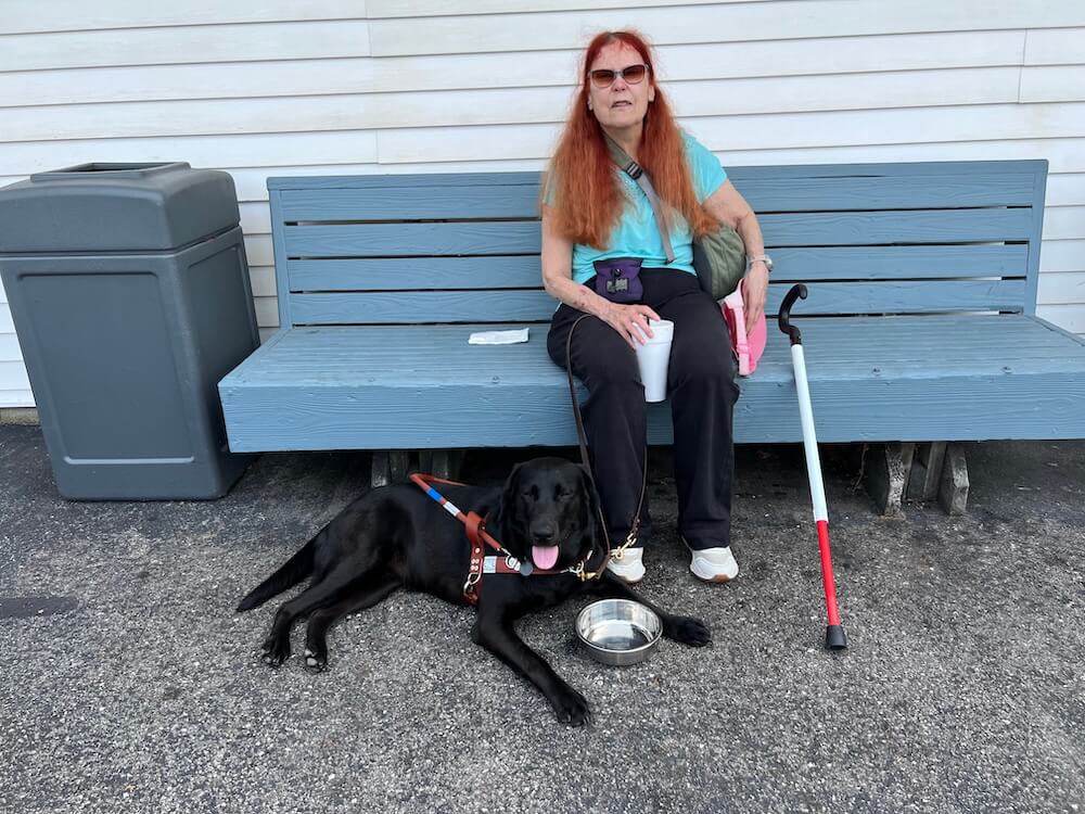 Mary Ann takes a break with a beverage sitting on a blue painted bench while JoJo happily lies next to a water dish