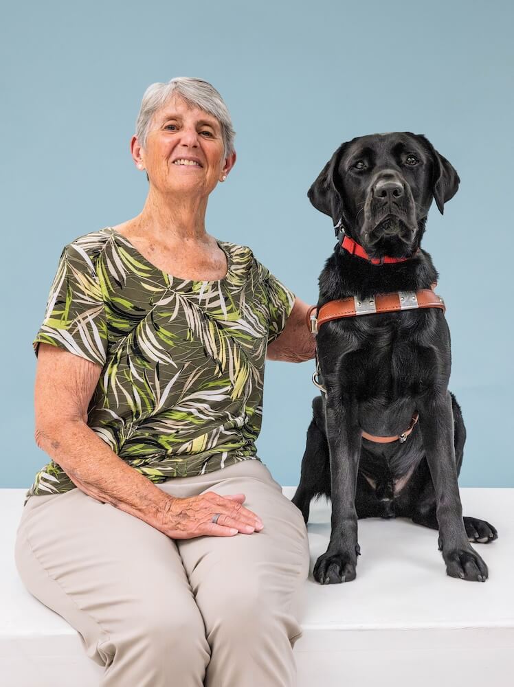 Robin and black Lab guide dog Yacht sit side by side for their team portrait against a pale blue background