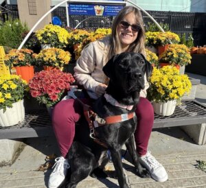 Kelsey sits on a bench with colorful fall mums and Java sits at her feet