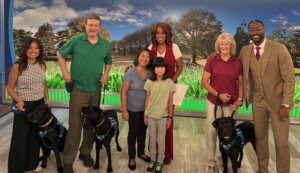 Raisers and dogs with hosts Gayle and Nate in front of segment backdrop