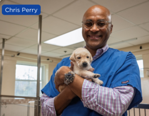 Chris Perry holding a small yellow puppy in the kennel