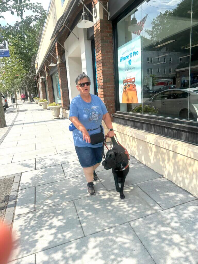 Elizabeth is led safely down a sidewalk past storefronts by guide dog Octavia