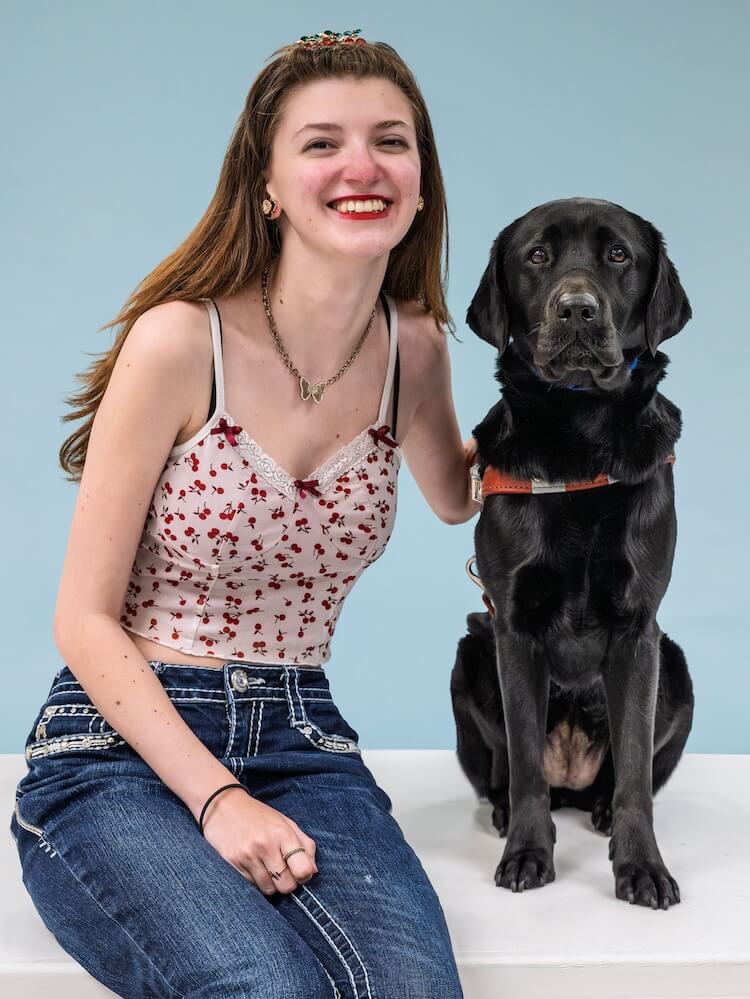 Kalia and black Lab guide dog Bethany sit against a pale blue background for their team portrait