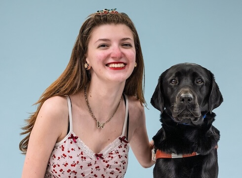 Kalia and black Lab guide dog Bethany sit against a pale blue background for their team portrait