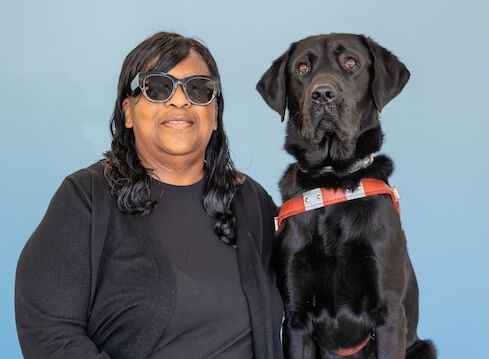 Cletus and black Lab guide dog Spunky sit against a pale blue background for their team portrait
