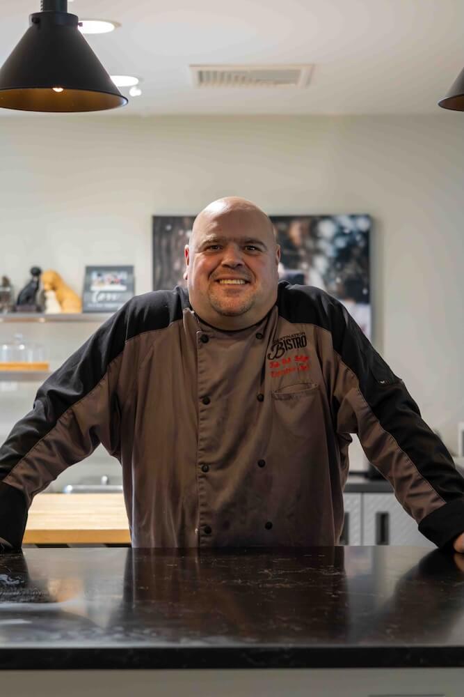 Chef Rob stands with his arms out and hands on the dark counter in the kitchen of Rosie's Cafe