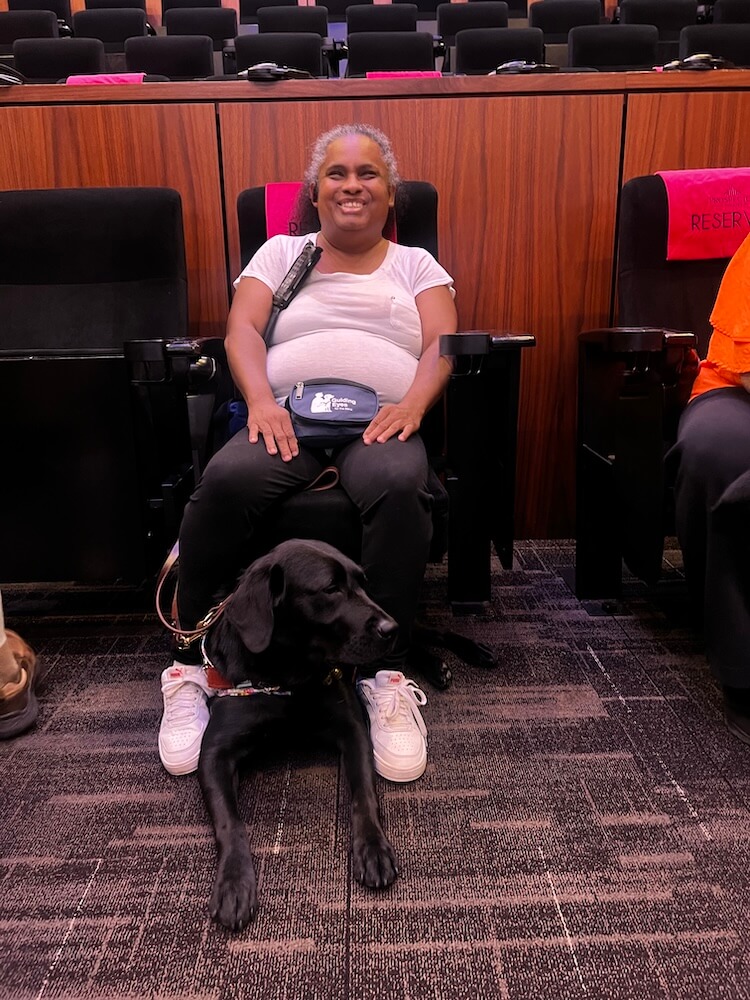 Natasha sits comfortably with Natasha at her feet at a movie with audio description