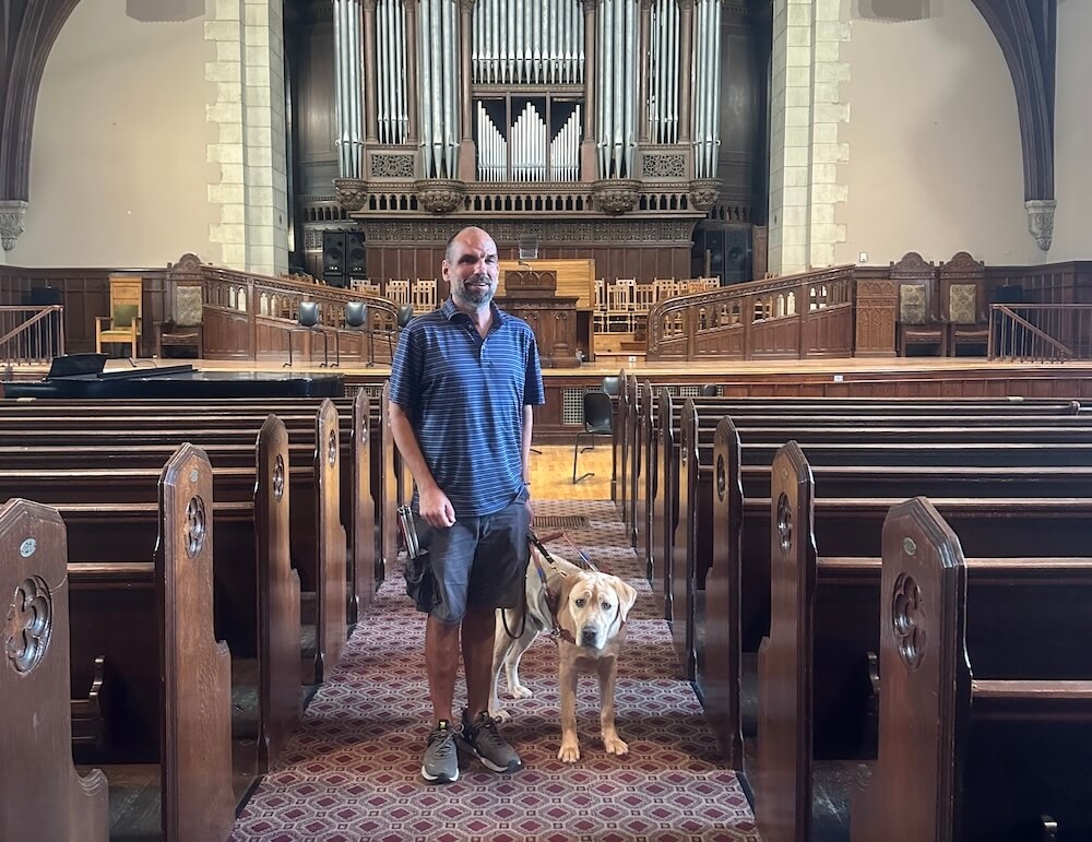Jim and guide Keanu stand in the aisle of the Vassar College chapel against the backdrop of the pipe organ and pulpit