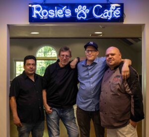 Under the blue neon sign for Rosie's Cafe stands Chef Rob and his team